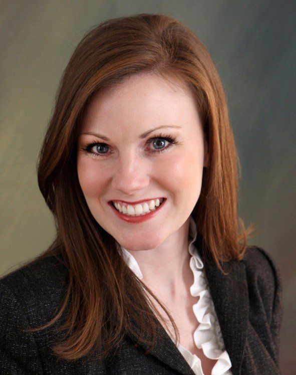 A woman wearing a black jacket and white ruffled blouse smiles for the camera